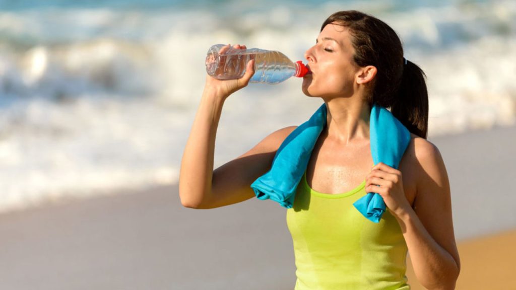 mulher na praia com garrafa de água